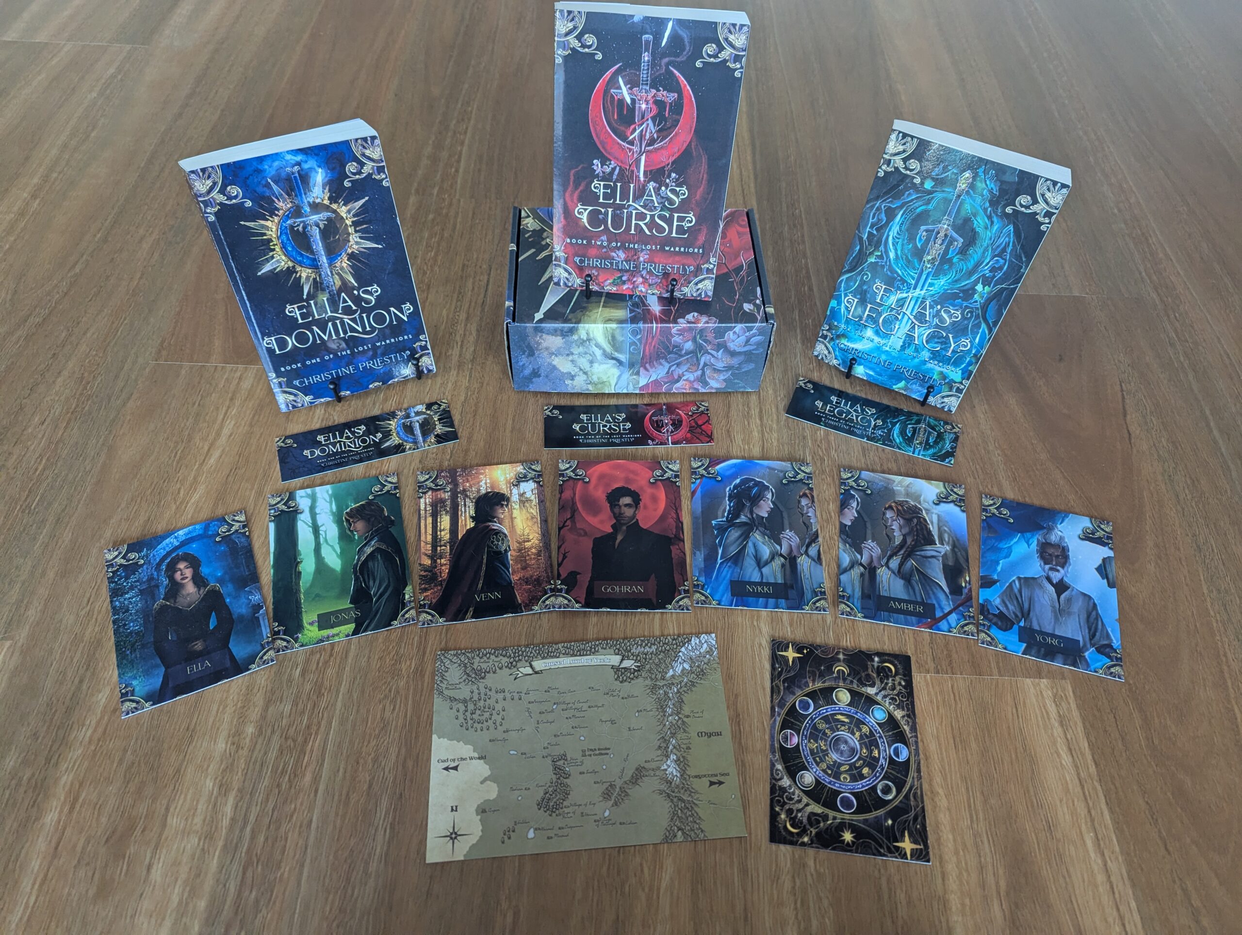 Photograph of Ella's Dominion, Ella's Curse and Ella's Legacy paperbacks along with custom book box, bookmarks, character art, map and magic chart